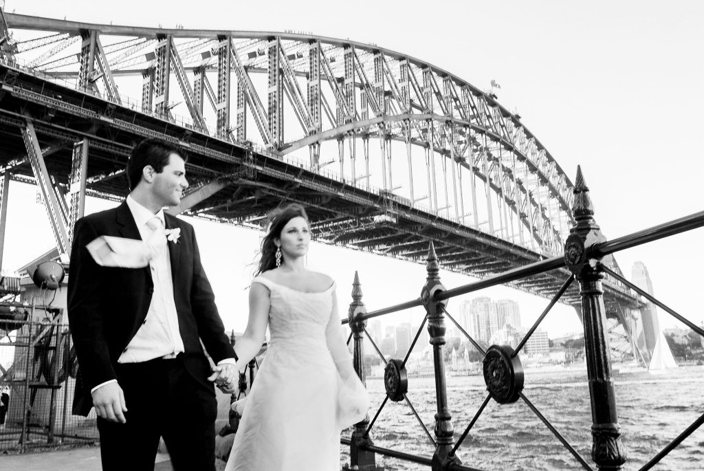 A wide angle Sydney Habour bridge view as a backdrop for bridal couple captured as iconic wedding photography by Arnold Szmerling, manifesting the enduring soul of the couple for the Visual Life Collection.