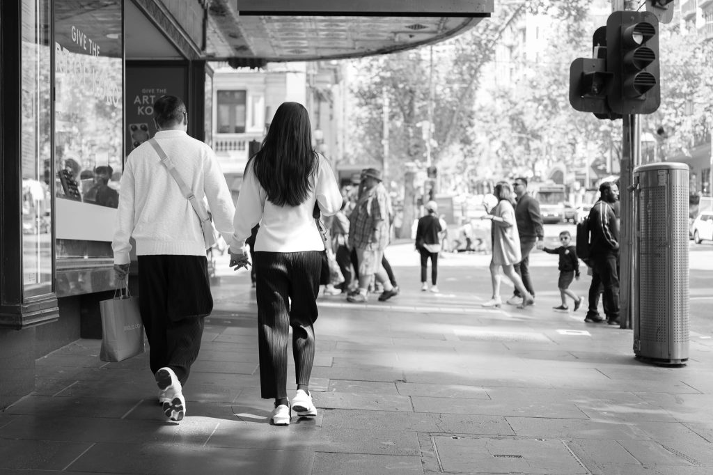 An elegant couple holding hands walking in Melbourne , a work of passion by Arnold Szmerling captured in Black and White during his Leica Q3 street photography experience.