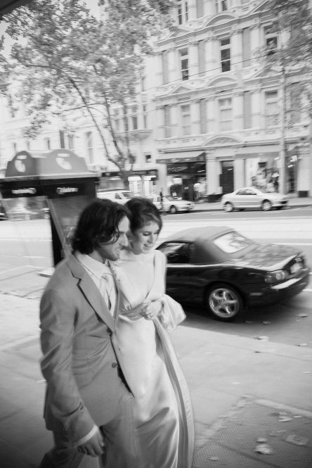 A street photography inspired editorial view of Bride and Groom walking in Collins Street Melbourne, captured as iconic wedding photography by Arnold Szmerling, manifesting the enduring soul of the couple for the Visual Life Collection.